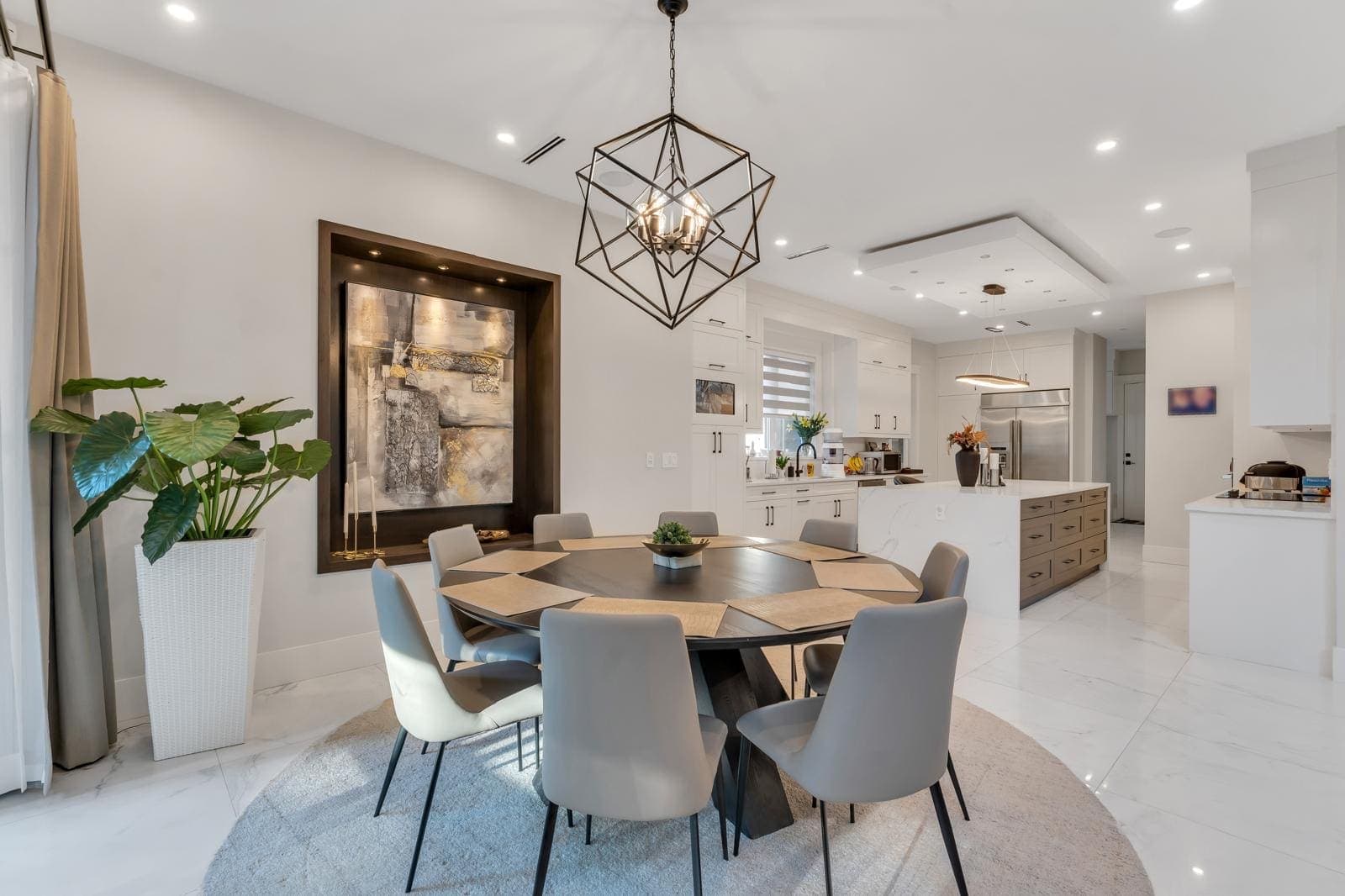Round dining table beneath a geometric pendant, kitchen island beyond — The Greenbelt House