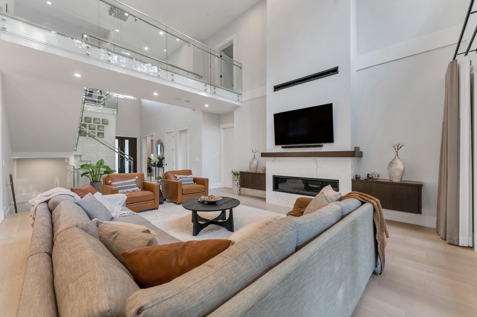 Living room looking back to the entry, stair and glass-railed landing — The Greenbelt House