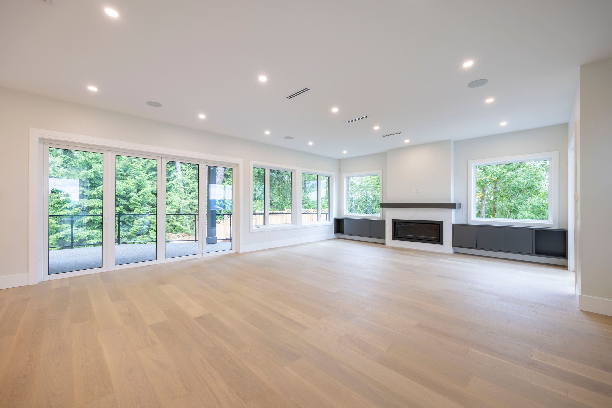 Living room along a full wall of windows with a linear fireplace — The Monashee House