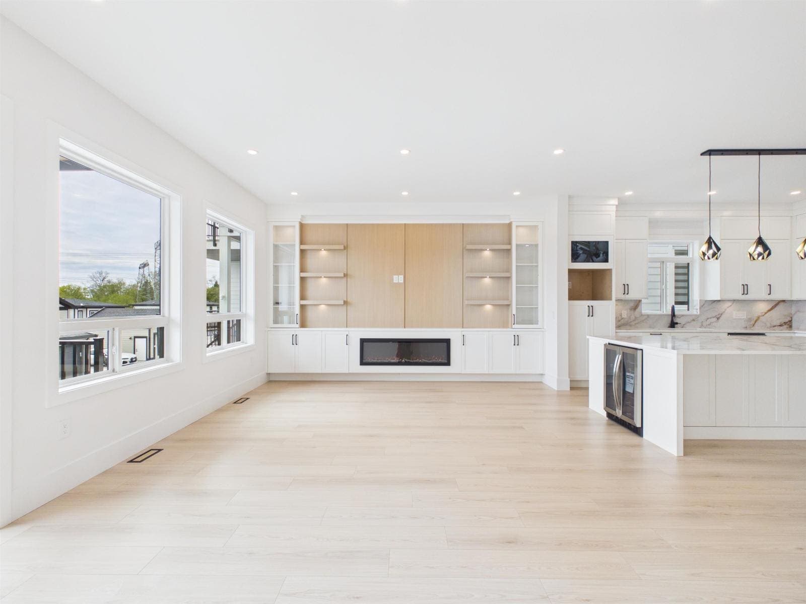 Open main floor — living room, linear fireplace and kitchen beyond — The Pacific Douglas Duplex