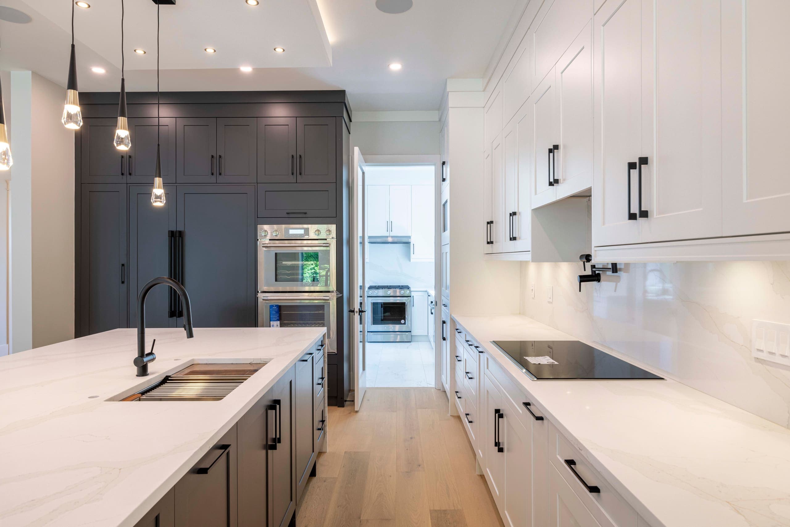 Kitchen detail — sink run, wall ovens and induction cooktop — The Ridge House